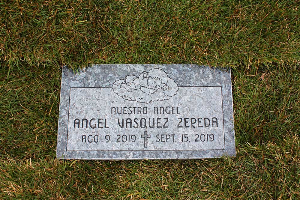 Blue granite child's marker with angel carving and Spanish lettering