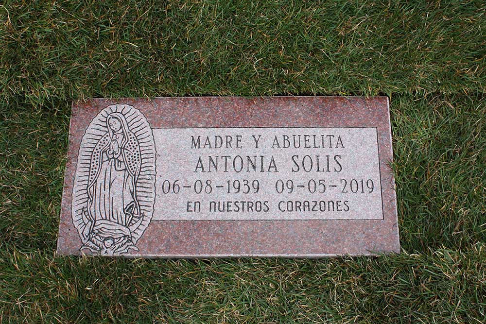 Red granite marker with our Lady of Guadalupe and Spanish text