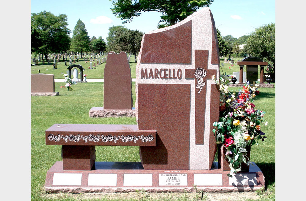 Red granite family monument with a carved cross and an integrated bench